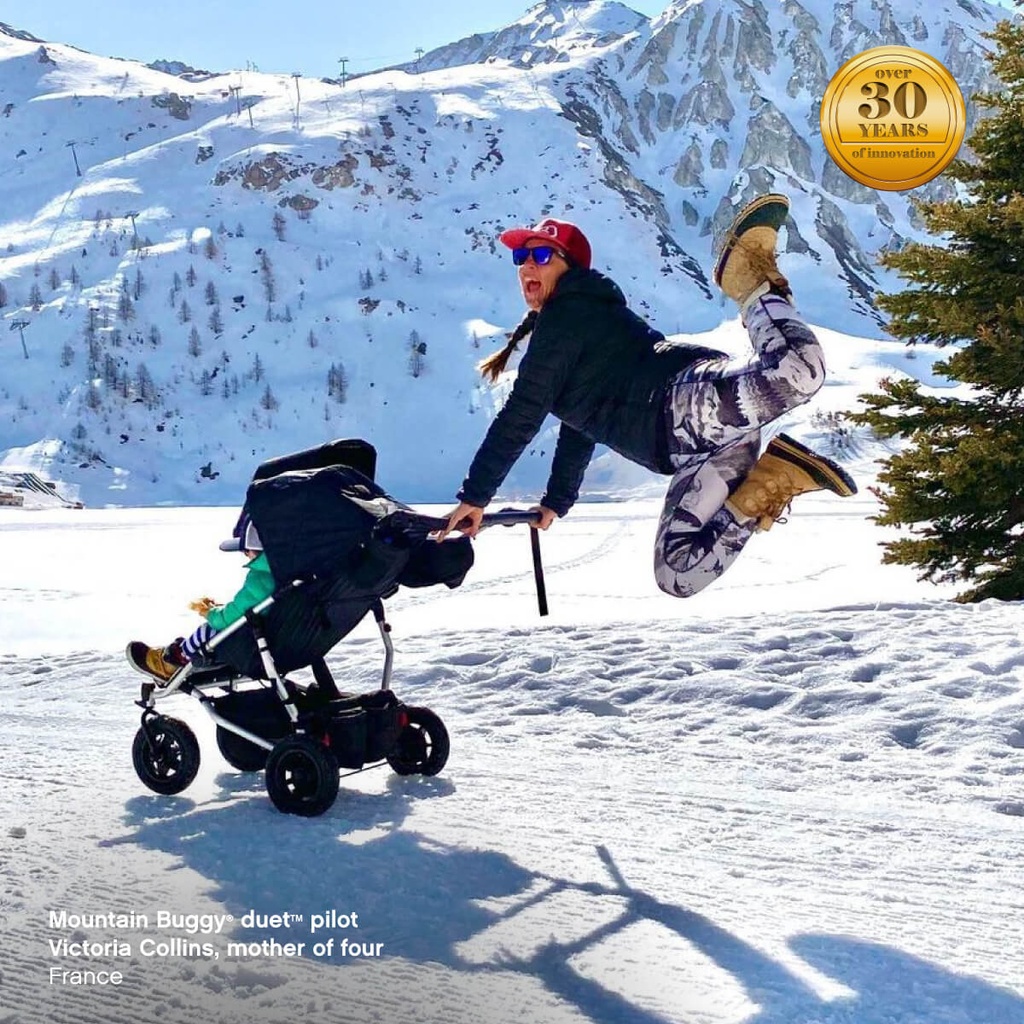 active mum pushing duet buggy while jumping for joy at the snow field - Mountain Buggy duet pilot Victoria Collins, mother of four, France